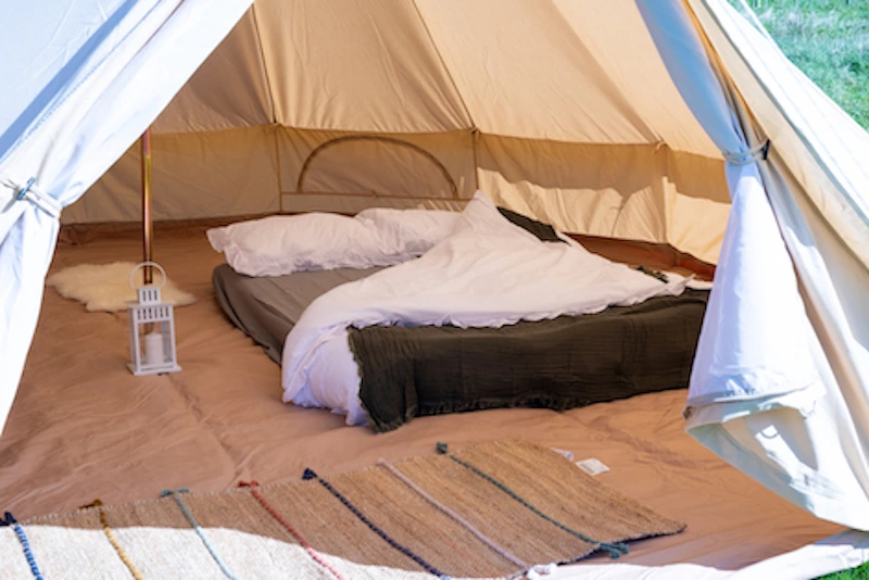 Interior of a luxury boutique glamping bell tent at Ditchling Camping, featuring a double bed with white linens and cozy rugs.