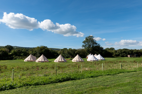 Group glamping circle of friends setup with bell tents arranged around a central fire pit with the South Downs in the distance