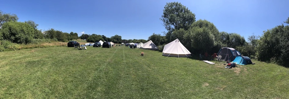 Panoramic view of grassy wild camping pitches with bell tents and campervans at a Ditchling campsite in the South Downs.