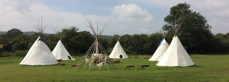 A circle of white tipis in a green field at Ditchling Camping, South Downs.