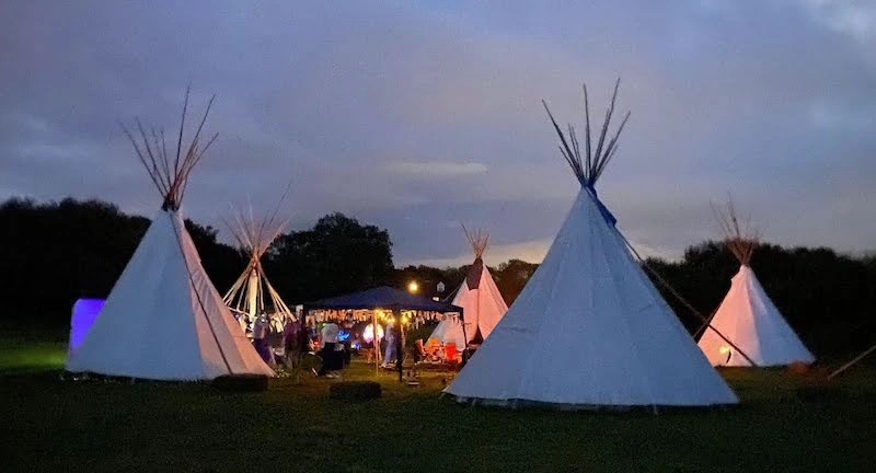 White event tipis illuminated at dusk for a private hire gathering at Ditchling Camping.